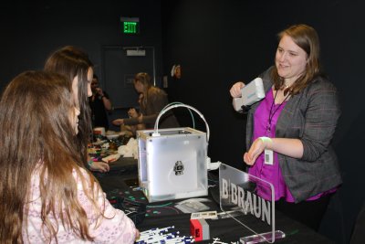 A woman working in a STEM profession shows two high school girls technology she uses in her field during the Women in Science & Engineering Career Connection Days.