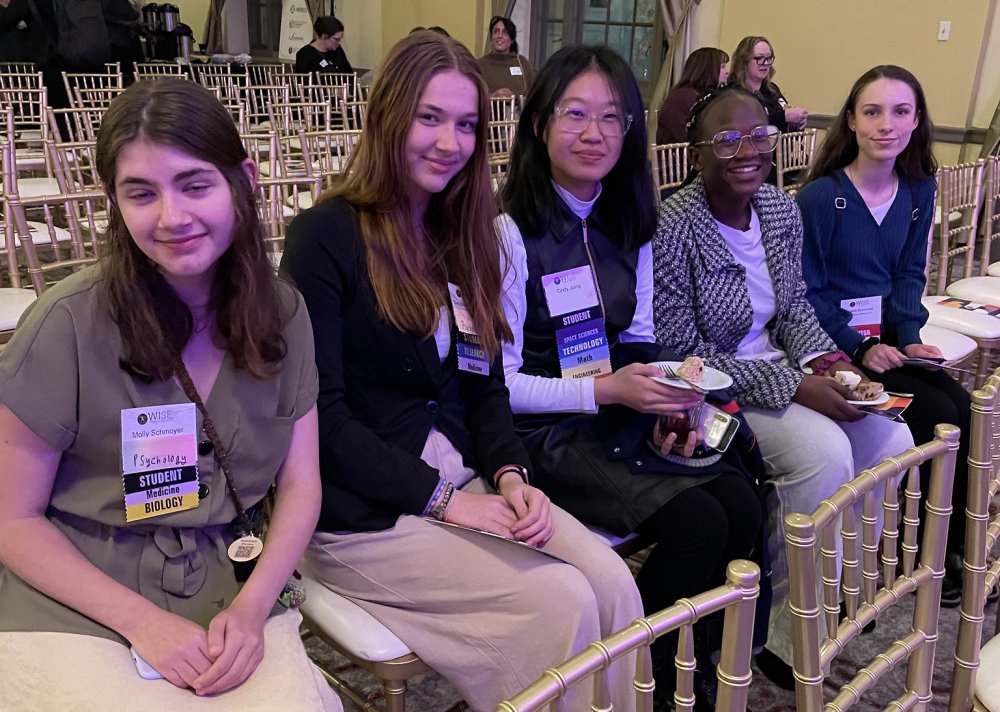 Five girls sitting in the audience awaiting the panel discussion to beginning at the Women in Science & Engineering (WISE) Forum.