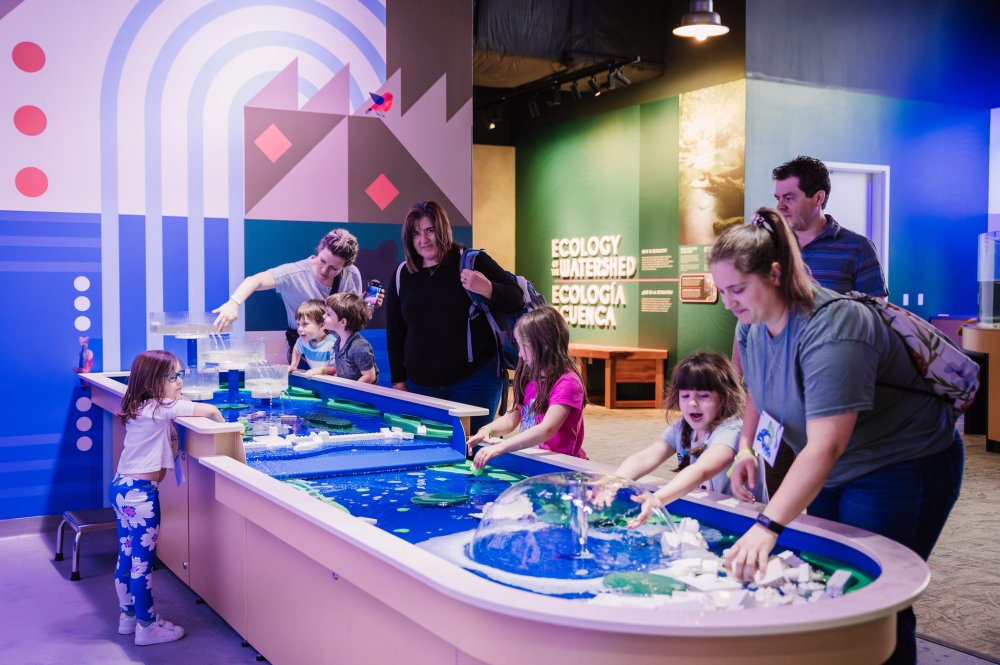 A group of children and parents play with the water table exhibit, which is included when you buy general admission tickets.